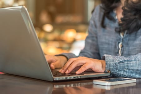 Close crop of a woman typing on her laptop, with her smartphone on the table next to her