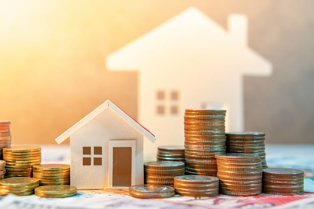 A miniature model of a house surrounded by stacks of quarters illustrating the financial aspect of buying a home.