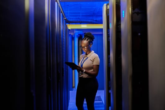 Woman reviewing information on a tablet standing in a room of servers.