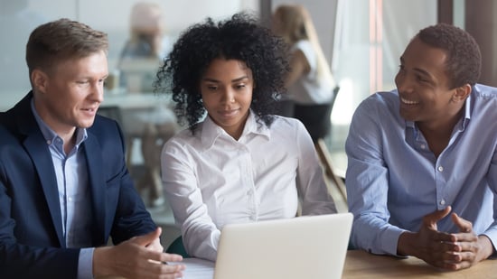 Three young professionals are focused on a laptop and working.