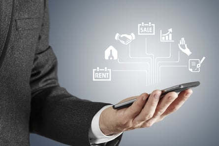 A professional man in a suit holds his phone in his palm which shows a projection of icons representing elements of a CRM